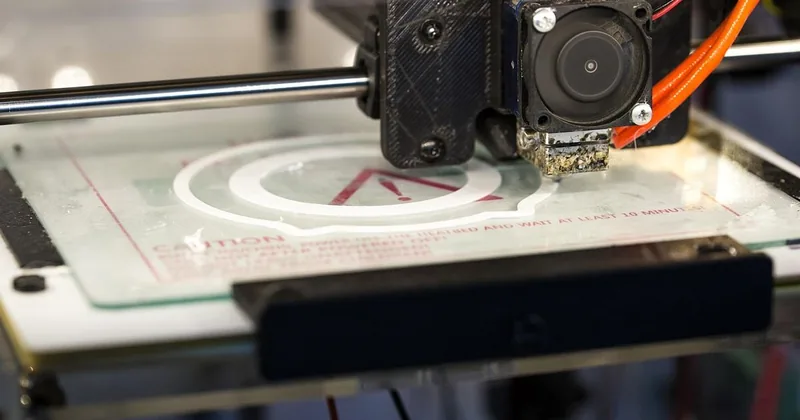 Imprimante 3D imprimant un logo avec filament orange sur plateau de fabrication